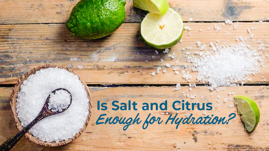 Overhead view of coarse sea salt in a wooden bowl and fresh lime slices on a wooden table, featuring the text "Is Salt and Citrus Enough for Hydration?"
